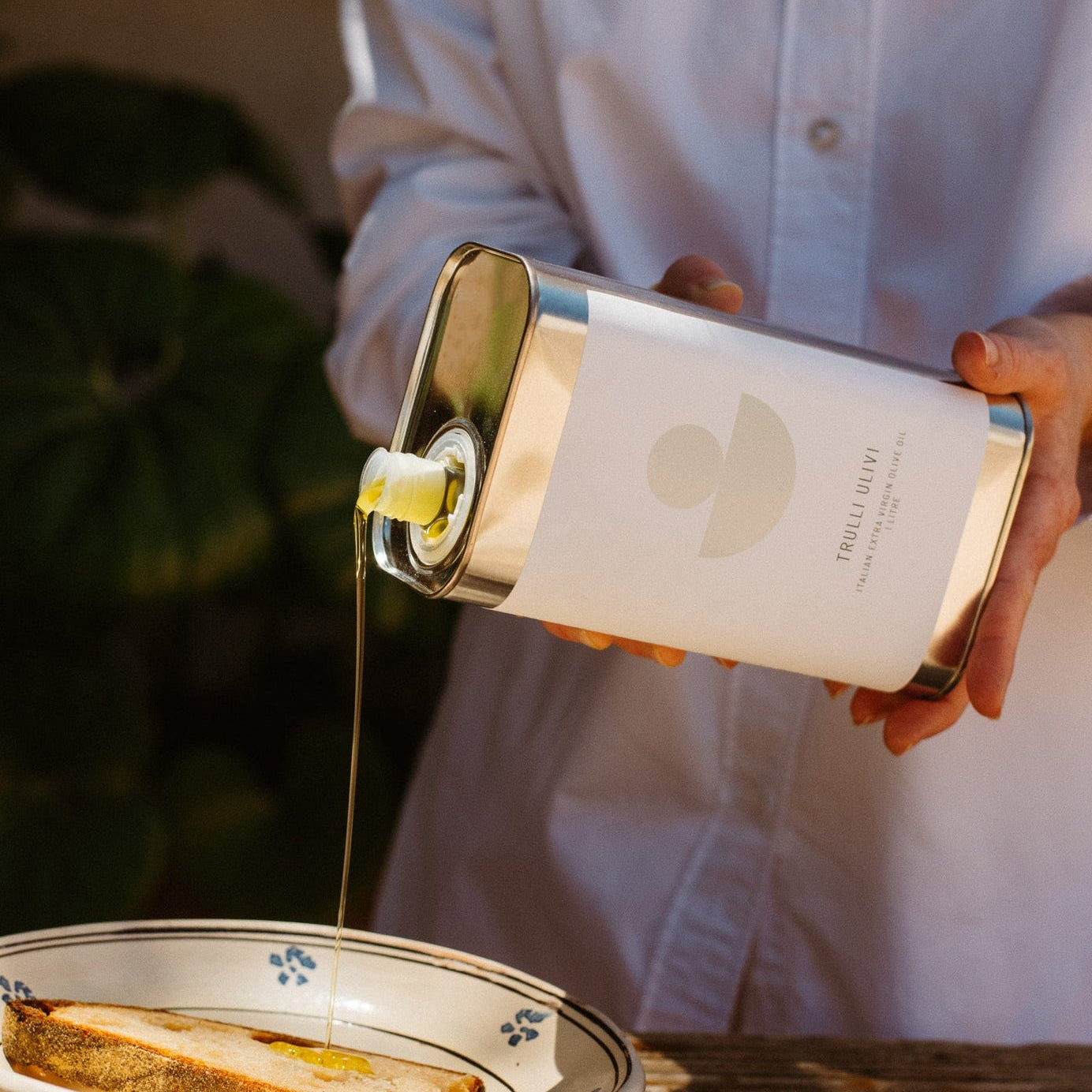 Person pouring olive oil from a bottle onto bread on a plate.
